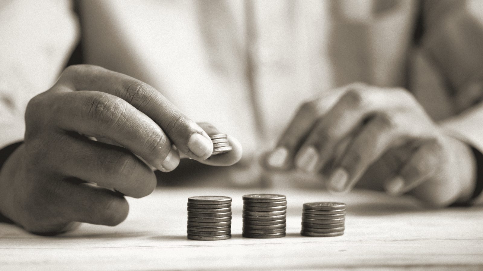 Una mano apila monedas en tres montones de distinta altura sobre una mesa
